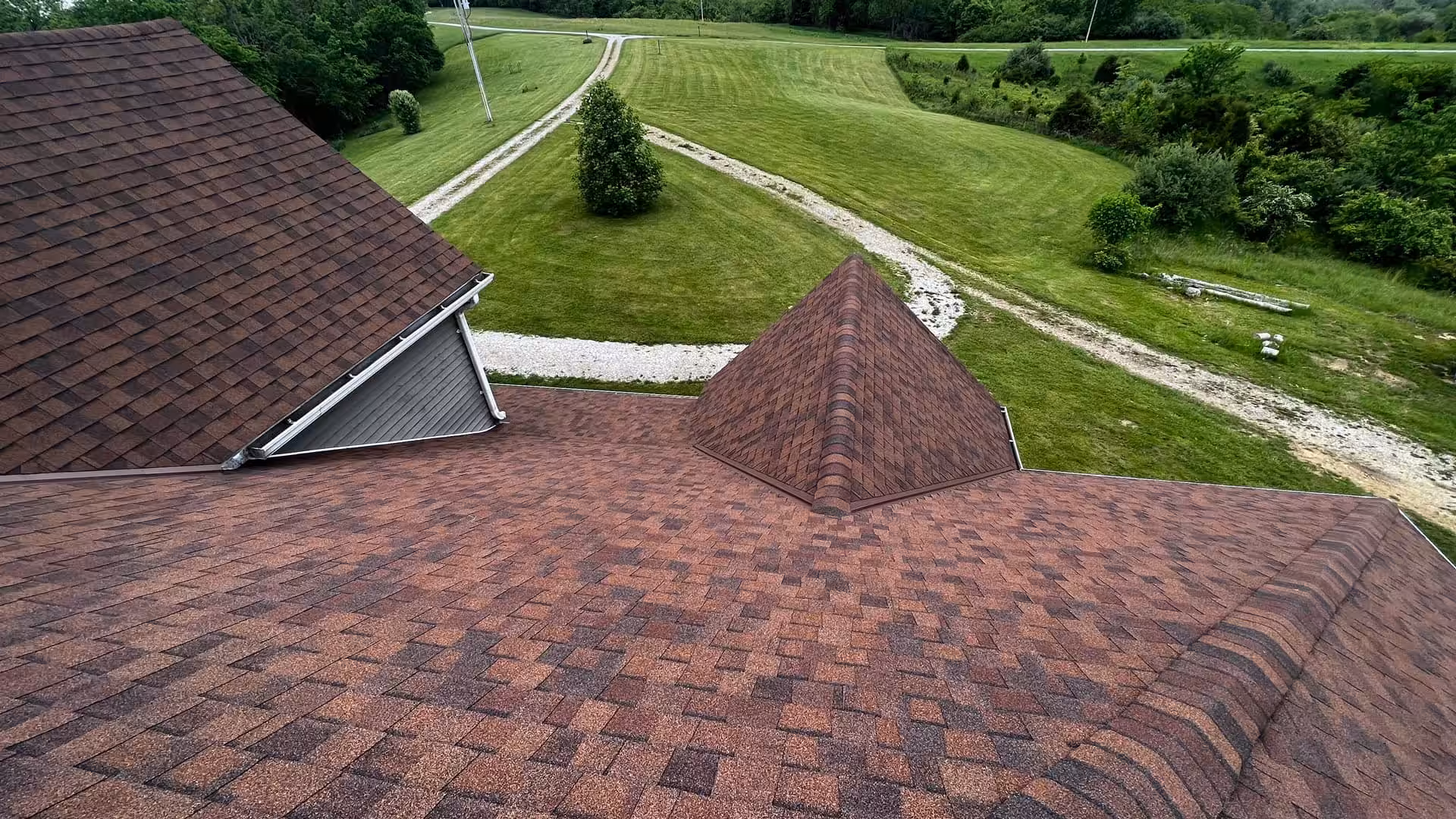 A new brown asphalt shingle roof installed on a home by Brandstetter's KangaRoof in Greater Cincinnati with green grass and trees in the background