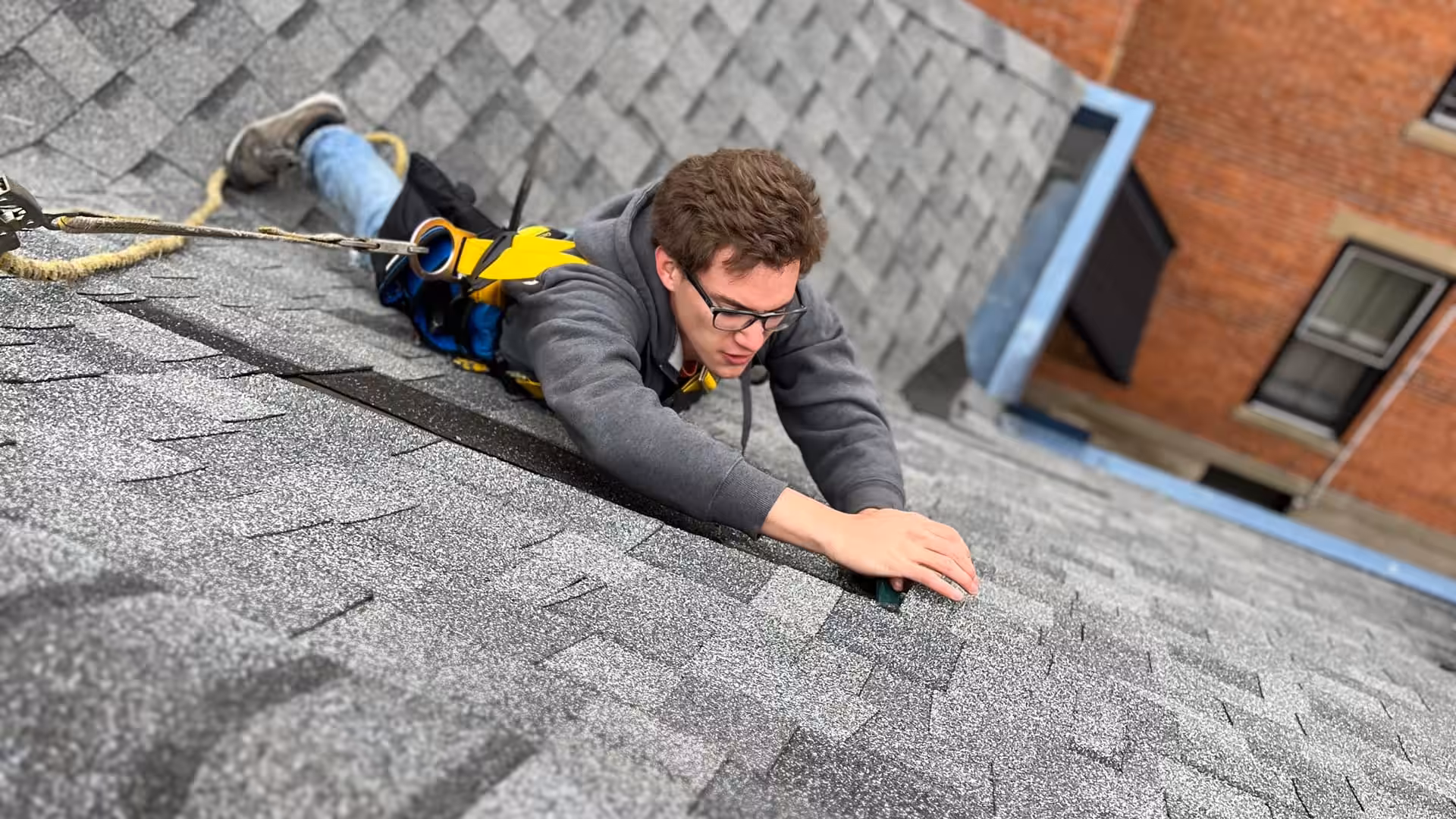 A Brandstetter's KangaRoof team member works on a roof with asphalt shingles