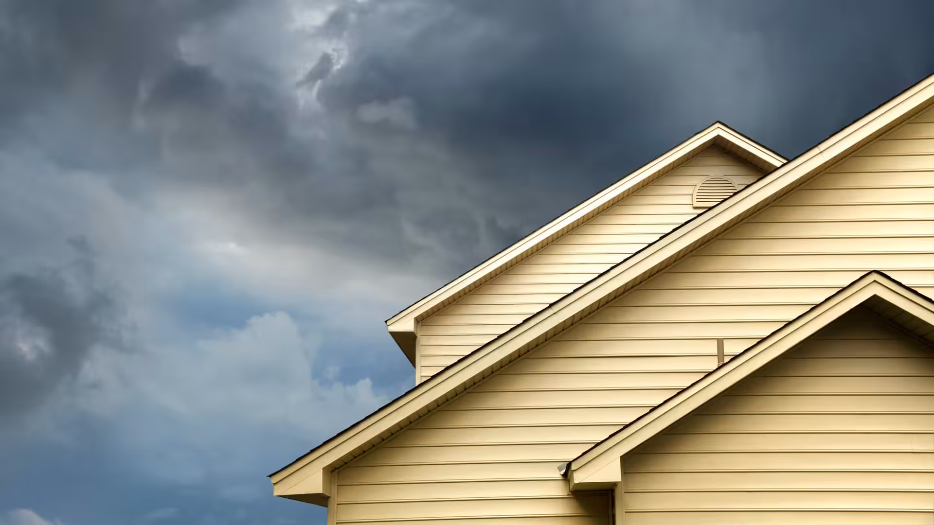 Side of house with siding repaired and replaced after storm, with stormy clouds in sky in the background