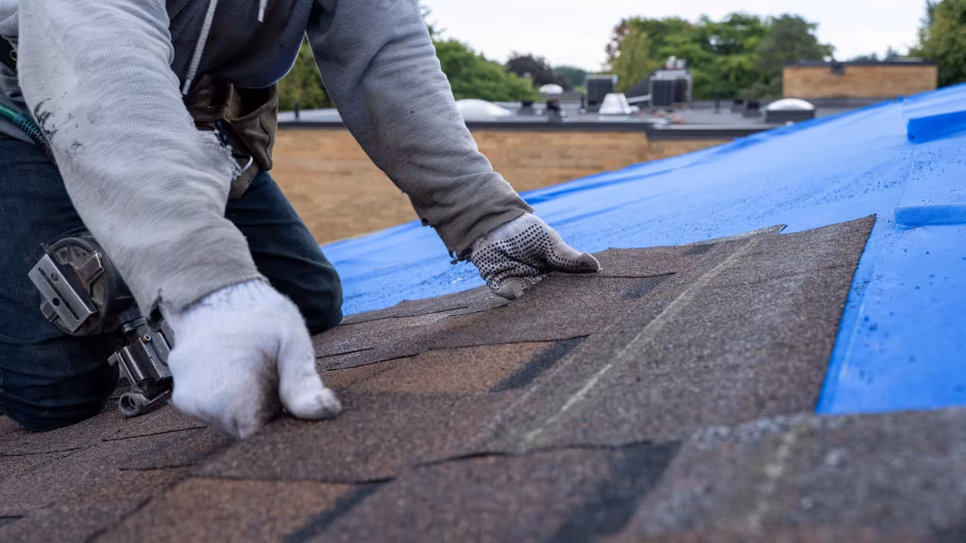 Close-up of a worker installing new asphalt shingles on a commercial building roof