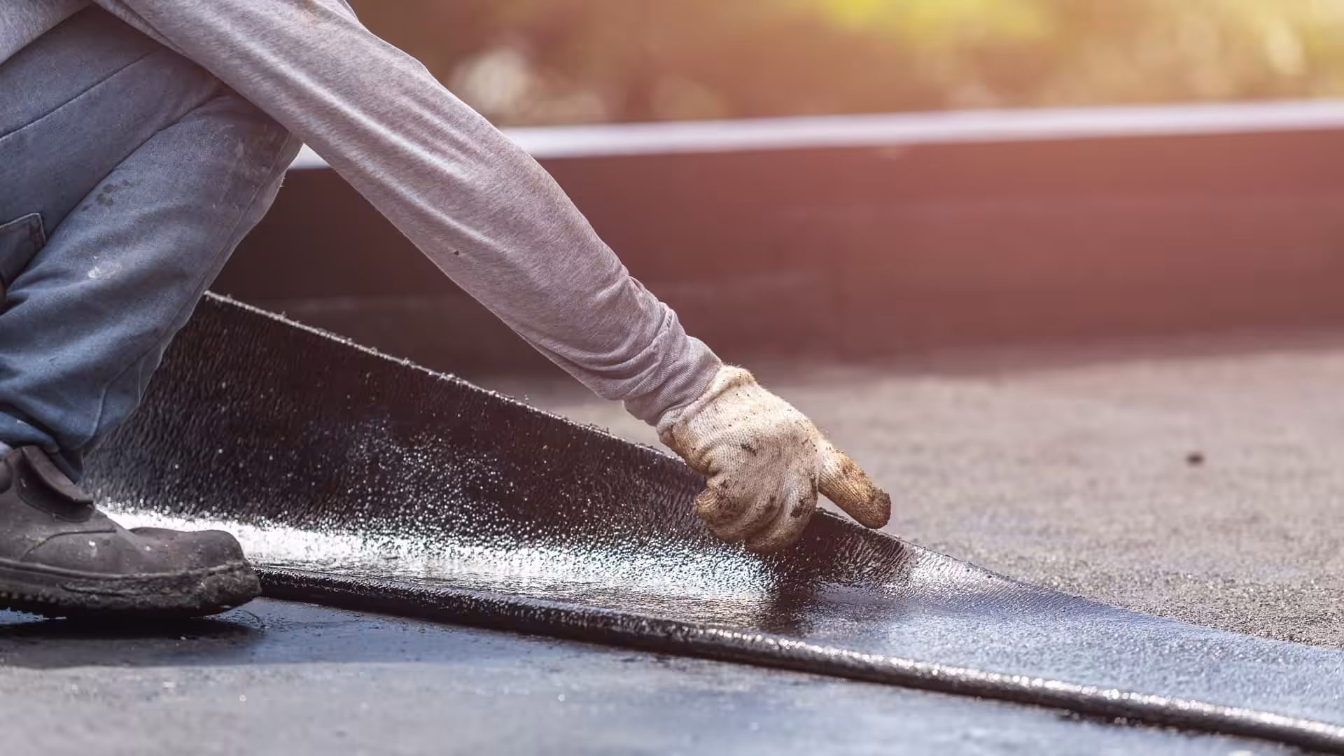 Close-up of a worker installing new tar strip roofing on a commercial building