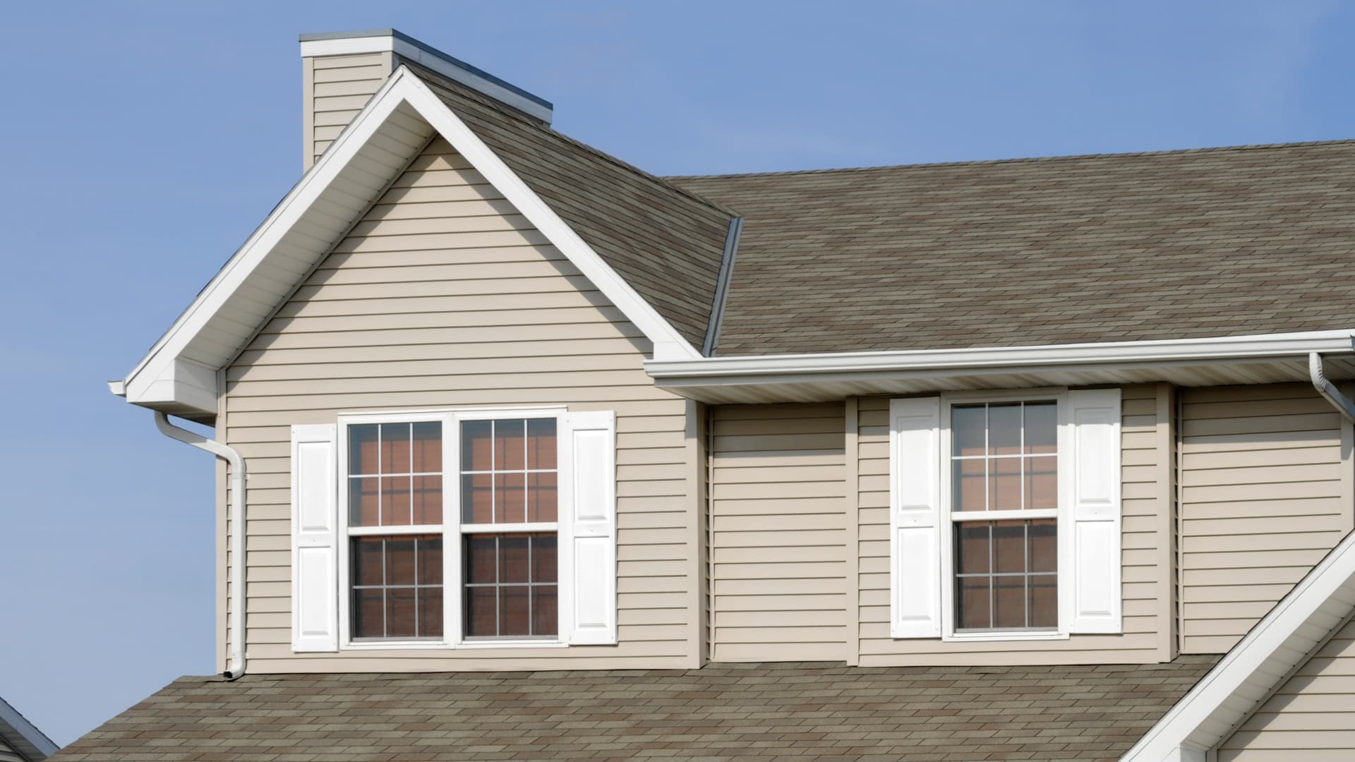Residential home with new siding, asphalt shingle roof, and clear blue sky in background