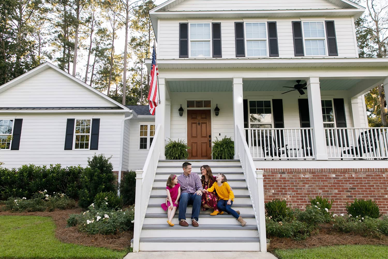 A family sitting on the steps of their older home.